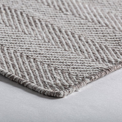 Primer plano de una alfombra rectangular de textura gris y beige con rayas diagonales, colocada sobre un suelo claro.