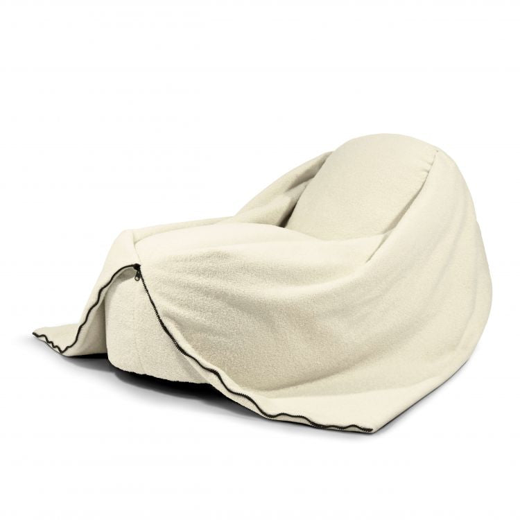 Un puff bean bag COCOON 100 TEDDY de color crema de tela borreguito (100×55×60 cm), con una manta a juego y borde de ribete negro, sobre un fondo blanco para mayor comodidad ergonómica en cualquier salón, dormitorio o sala de juegos.