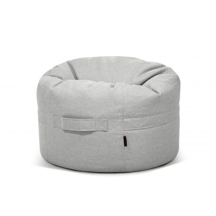 Sobre un fondo blanco liso se muestra un puf ROLL 80 RIVIERA gris claro, de 80×80×35 cm, fabricado en tejido hidrófugo y antimanchas para uso en interiores y exteriores, con asa lateral.