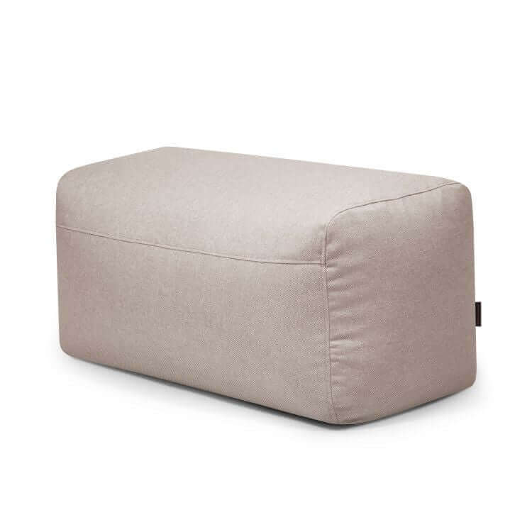 El Pouf Plus 100 Riviera es un puf rectangular de tela beige claro con bordes redondeados para uso en exteriores, ideal como reposapiés versátil o asiento extra, mostrado sobre un fondo blanco liso.