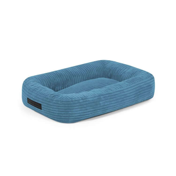 La Cama para perro de terciopelo acanalado 55×45×16 cm - DOG BED 55 WAVES presenta laterales elevados y una base plana acolchada en terciopelo azul, perfecta como elegante colchón para perros. Se muestra sobre fondo blanco.