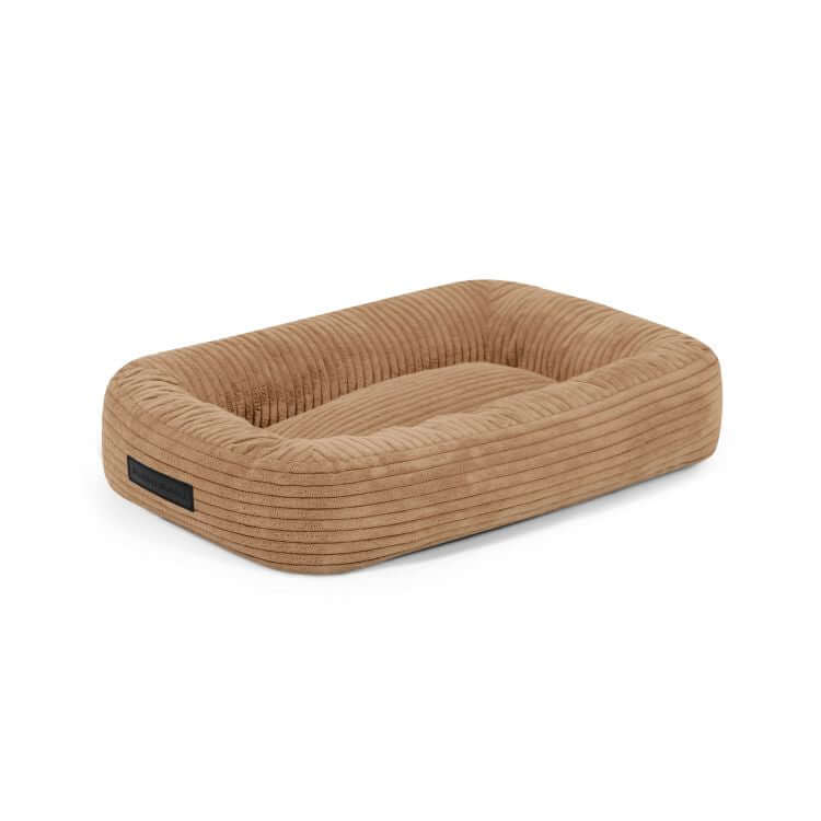 La Cama para perro de terciopelo acanalado 55×45×16 cm - DOG BED 55 WAVES presenta un diseño rectangular de color marrón claro con bordes elevados y un centro rebajado para mayor comodidad, que se muestra sobre un fondo blanco liso.