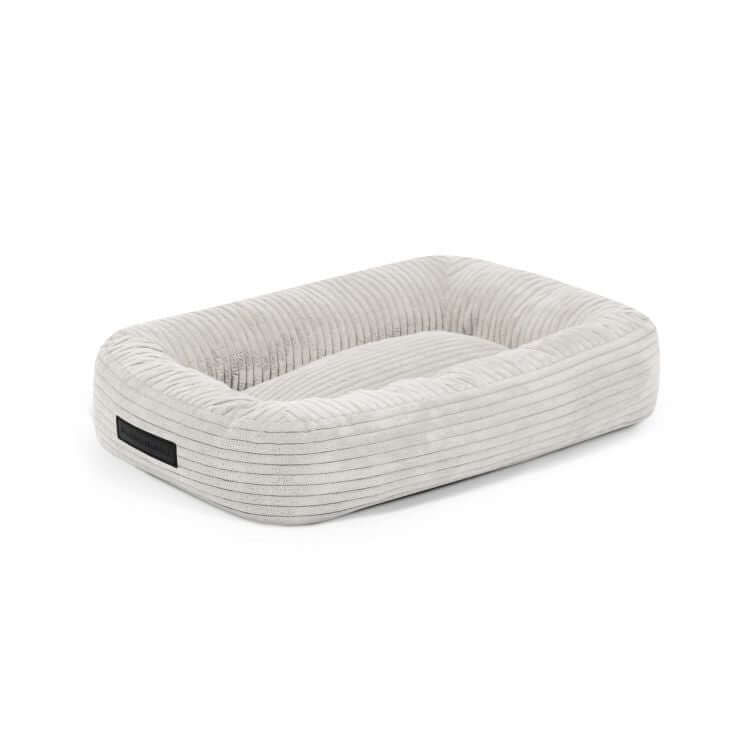 La Cama para perro de terciopelo acanalado 55×45×16 cm - DOG BED 55 WAVES es una cama rectangular de color gris claro con bordes elevados y base acolchada, ideal como acogedor colchón para perros pequeños.