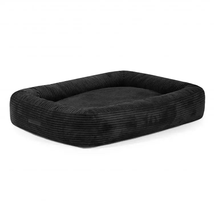 Cama para perro de terciopelo acanalado (100×70×20 cm), rectangular, negra, con bordes elevados y centro plano y acolchado, sobre fondo blanco.
