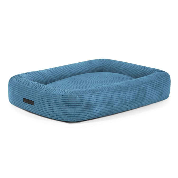 Cama para perro de terciopelo acanalado DOG BED 100 WAVES (100×70×20 cm), rectangular, azul, con laterales elevados y cojín plano central, sobre fondo blanco.