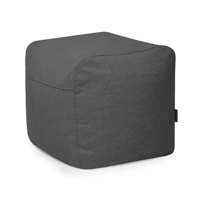 El Pouf Plus 50 Casa es un puf ergonómico en forma de cubo, con bordes redondeados y funda lavable, revestido de tela, de color gris oscuro, diseñado para su uso en exteriores y que se muestra sobre un fondo blanco liso.