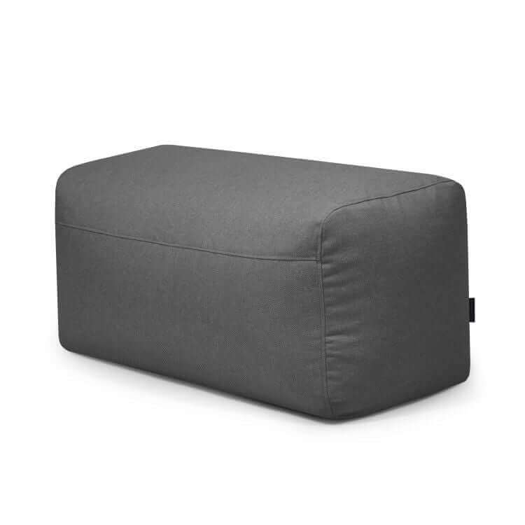 El Pouf Plus 100 Riviera es un puf rectangular de tela gris oscuro para exteriores con bordes redondeados, perfecto como reposapiés versátil o asiento adicional, mostrado sobre fondo blanco.