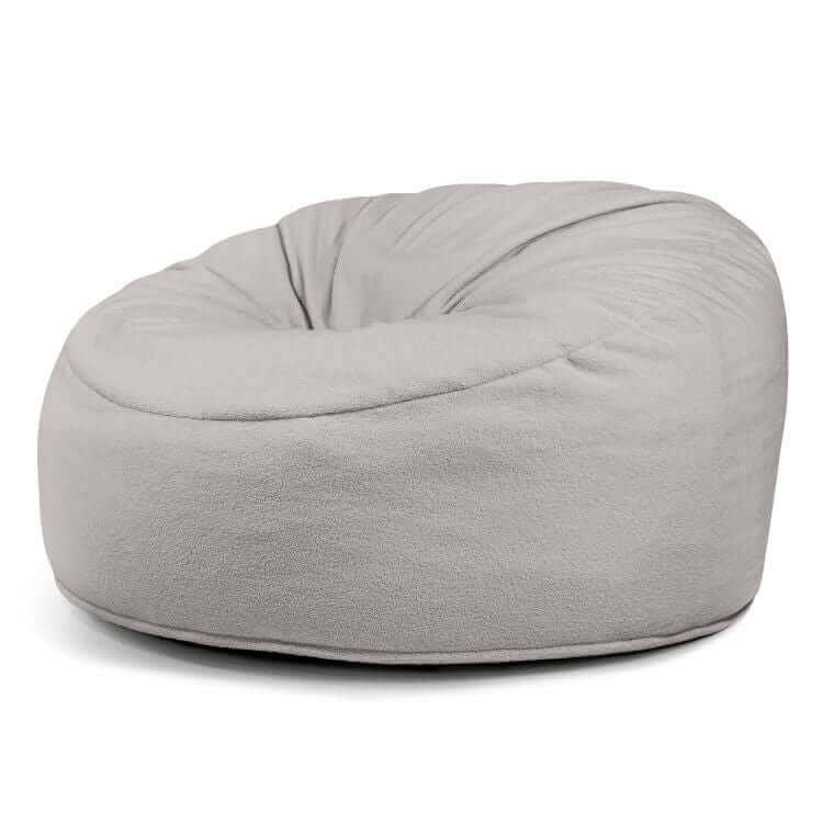 El Foam Bean Bag Om 135 Teddy para exterior es un sillón redondo de color gris claro con una suave funda de tela que ofrece un confort ergonómico, presentado sobre un fondo blanco.