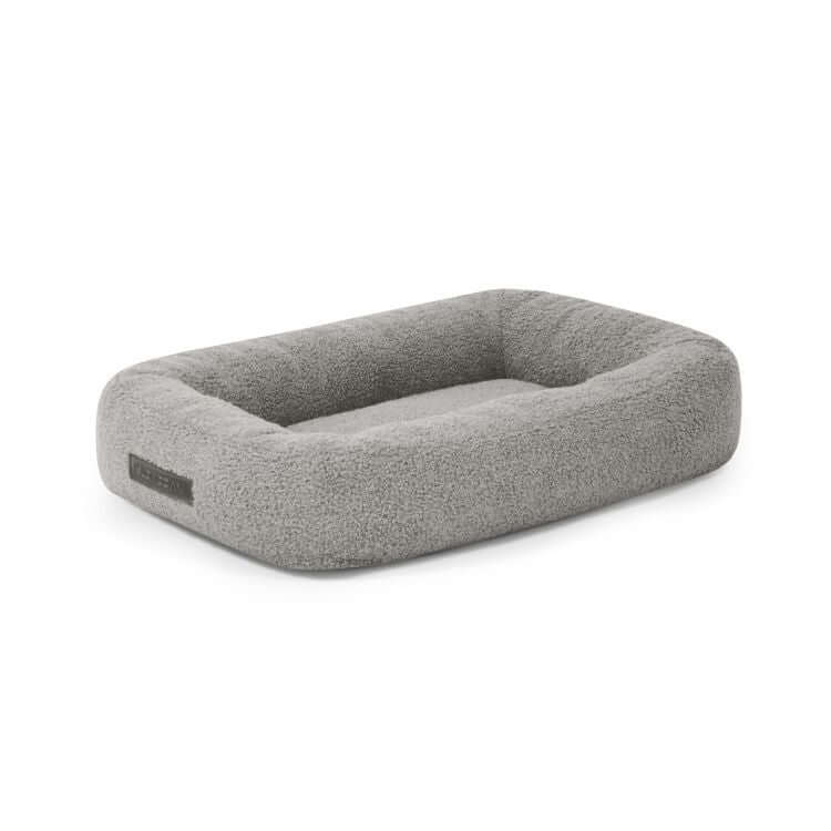 La Cama para perro de tela borreguito 55×45×16 cm - DOG BED 55 TEDDY es una cama rectangular para perros de color gris claro, con laterales elevados y una superficie suave y texturizada, que ofrece un confort afelpado a tu mascota.