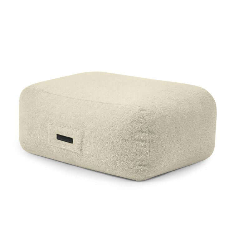 Moderno puf de espuma beige SNUG 83 TEDDY, tapizado en suave tejido borreguito (85×68×40 cm), ideal para salón o dormitorio; cuenta con una pequeña etiqueta negra y es un asiento versátil para cualquier espacio.