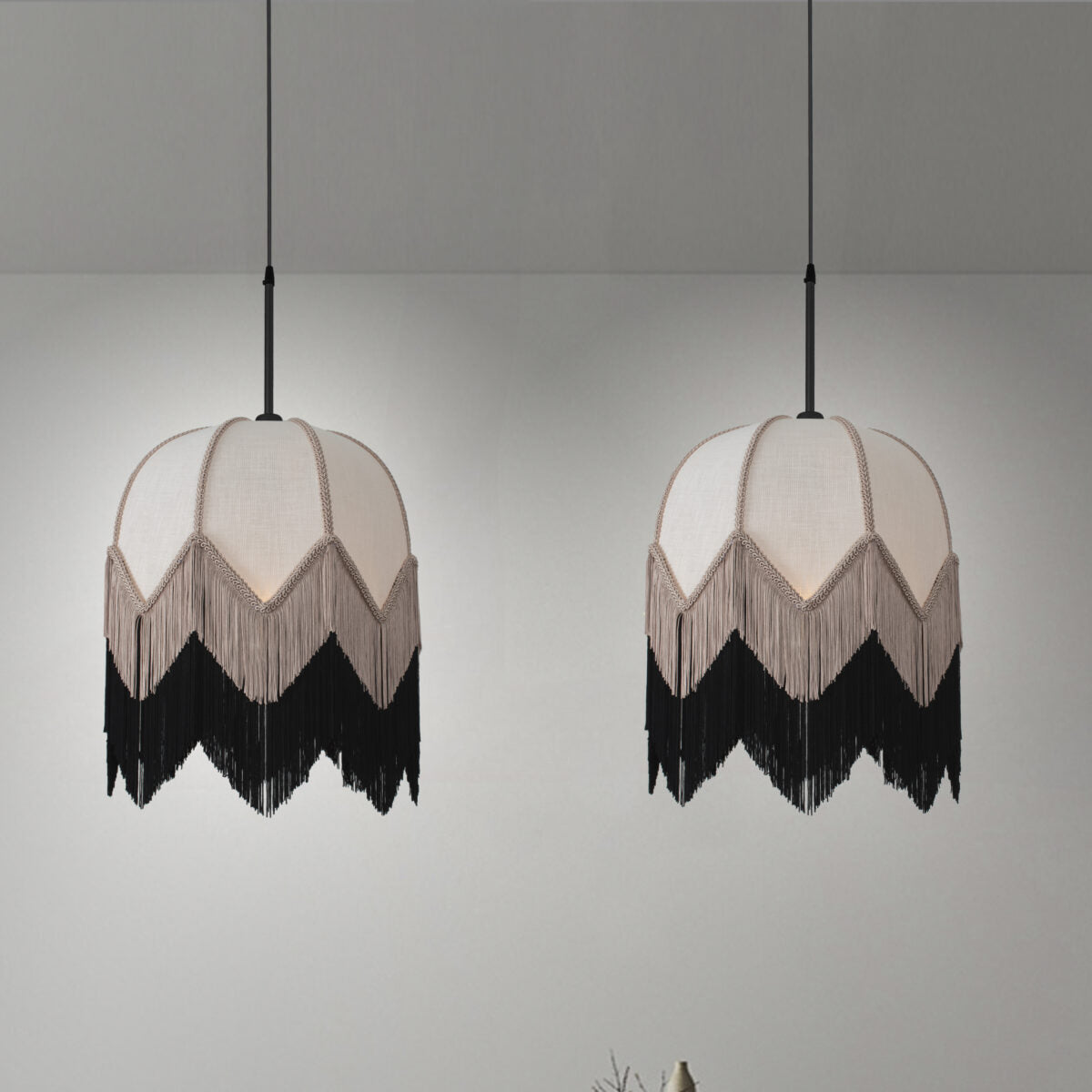 Dos elegantes lámparas colgantes, la Lámpara colgante con flecos vintage B-Cruda, cuelgan del techo con pantallas en forma de cúpula con flecos contra una pared lisa, mostrando un encantador estilo vintage.