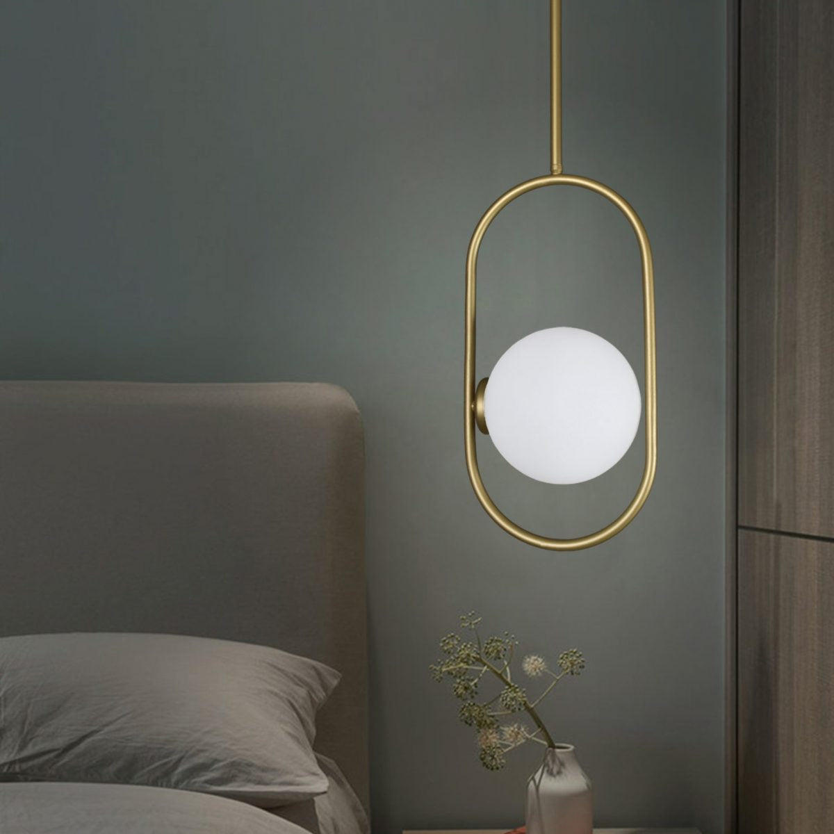 Un dormitorio moderno con una cama gris y una mesita de noche con un florero se ve realzado por la Lámpara de Techo Colgante Moderna 3135-1C, que muestra una estética industrial-chic con su luz colgante dorada y su globo blanco.