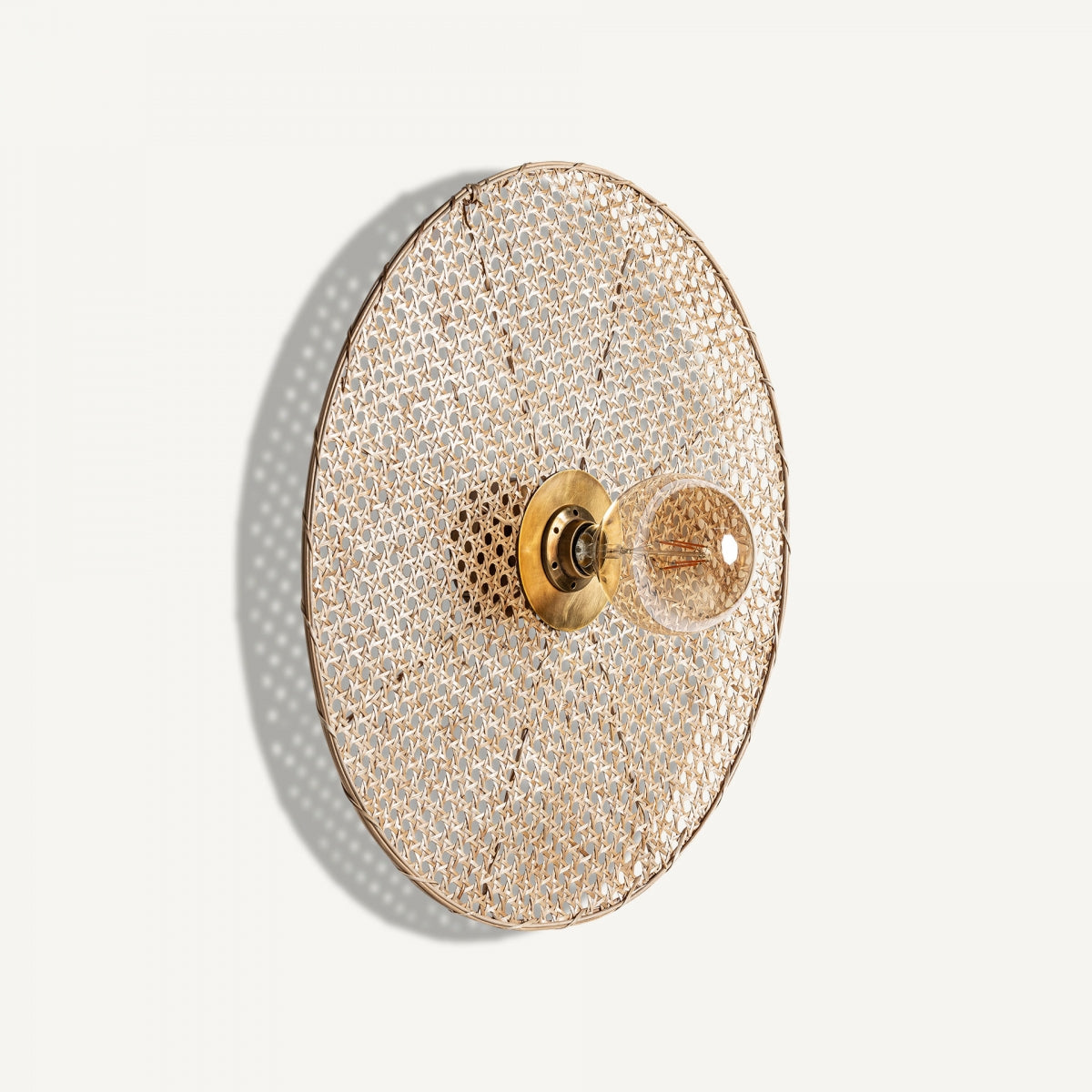 El aplique de pared en hierro y ratán Macey destaca por su diseño elegante con pantalla circular tejida y bombilla expuesta, ideal para dar un toque contemporáneo a paredes blancas.