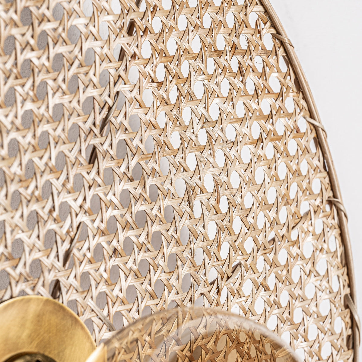 Primer plano del patrón de ratán tejido en un marco circular, que muestra el Aplique de pared en hierro y ratán Macey con su elegante diseño, accesorio de latón y un detalle de vidrio visible en la esquina inferior.
