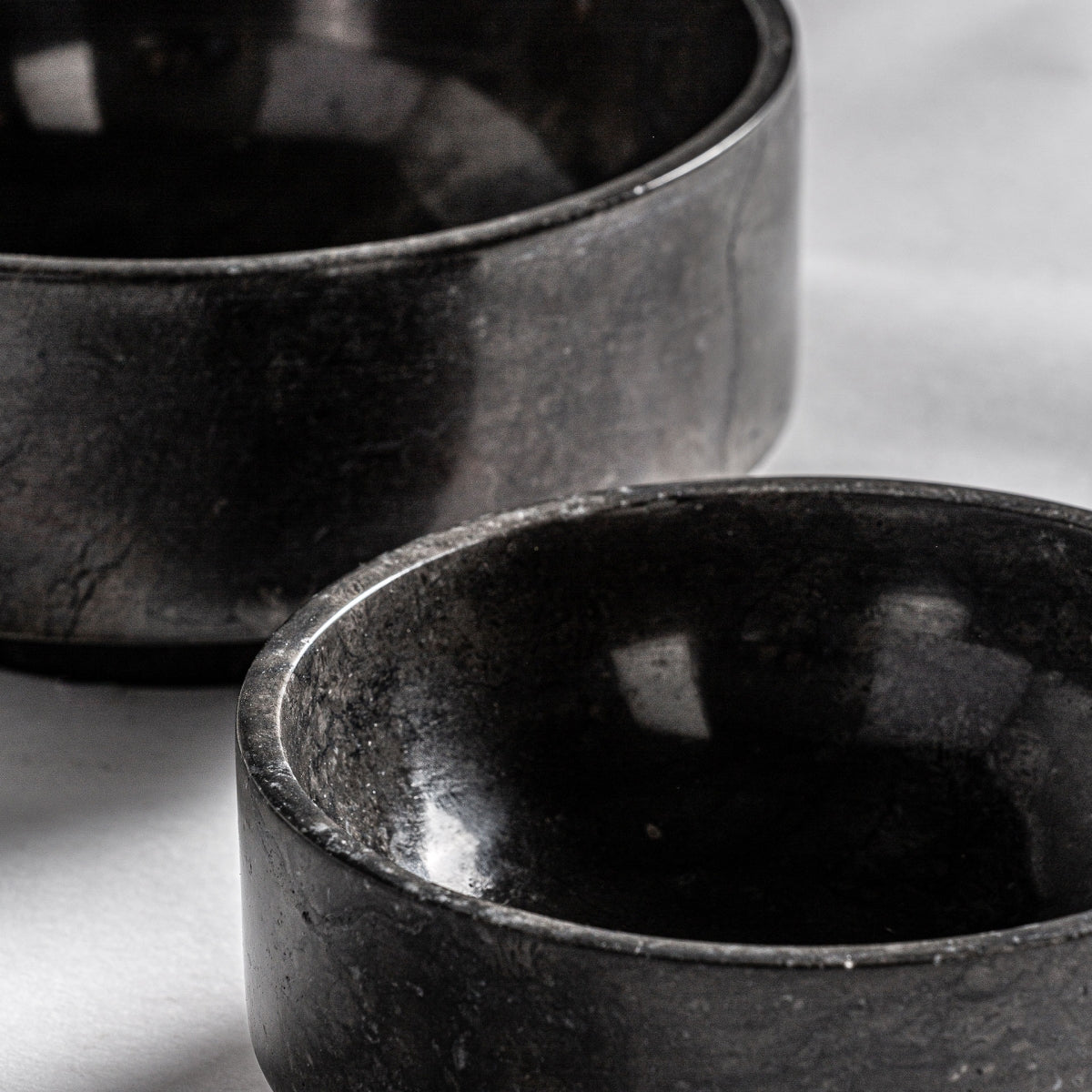 Las dos piezas del Centro de mesa en mármol negro Nora están juntas sobre una superficie blanca, con un tazón parcialmente superpuesto al otro, creando un diseño elegante ideal como centro de mesa.