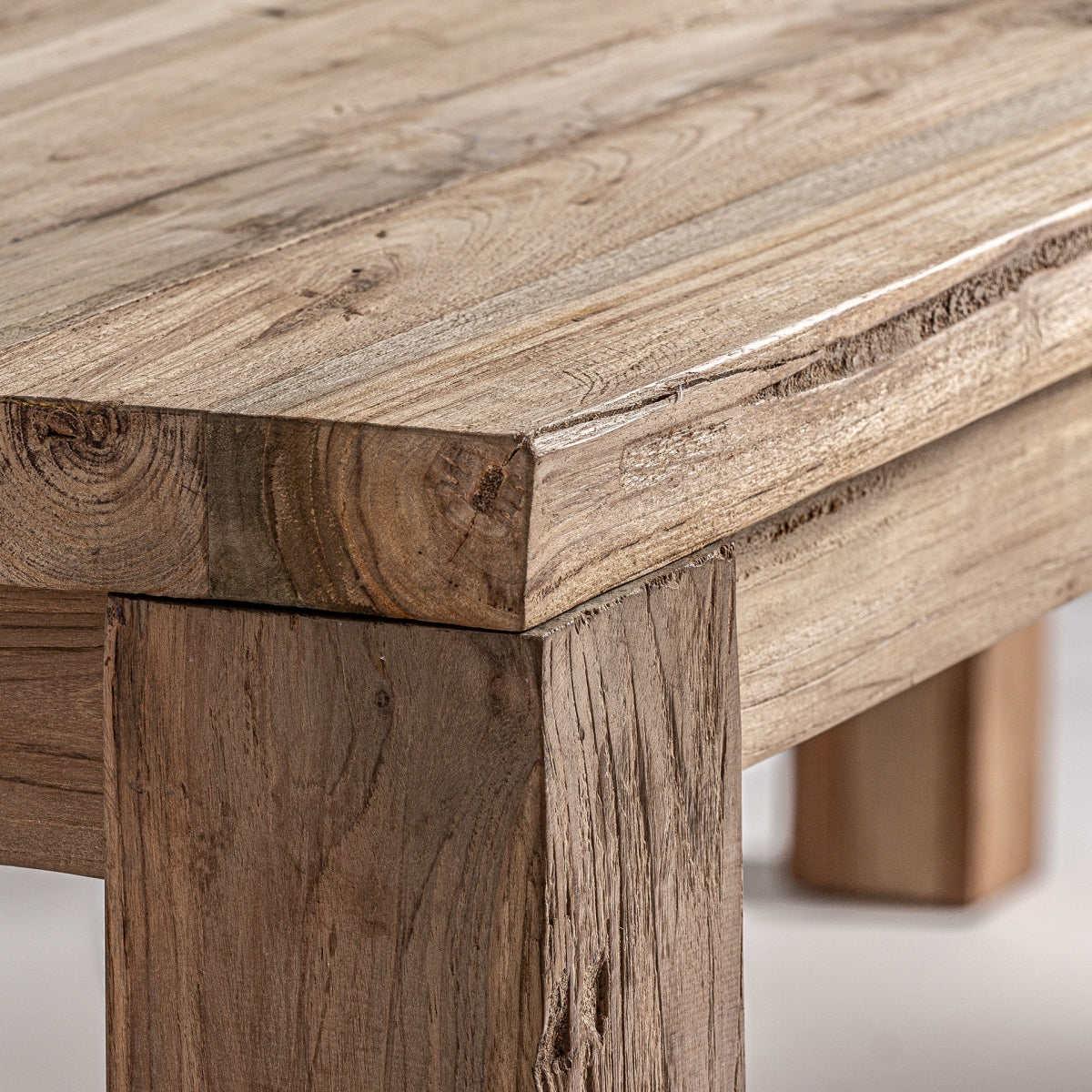 Primer plano de una mesa esquinera de madera con vetas y juntas detalladas. La mesa de comedor de madera de teka reciclada Lux ofrece un aspecto natural y natural con texturas de madera visibles, diseñada para un aspecto ecológico.