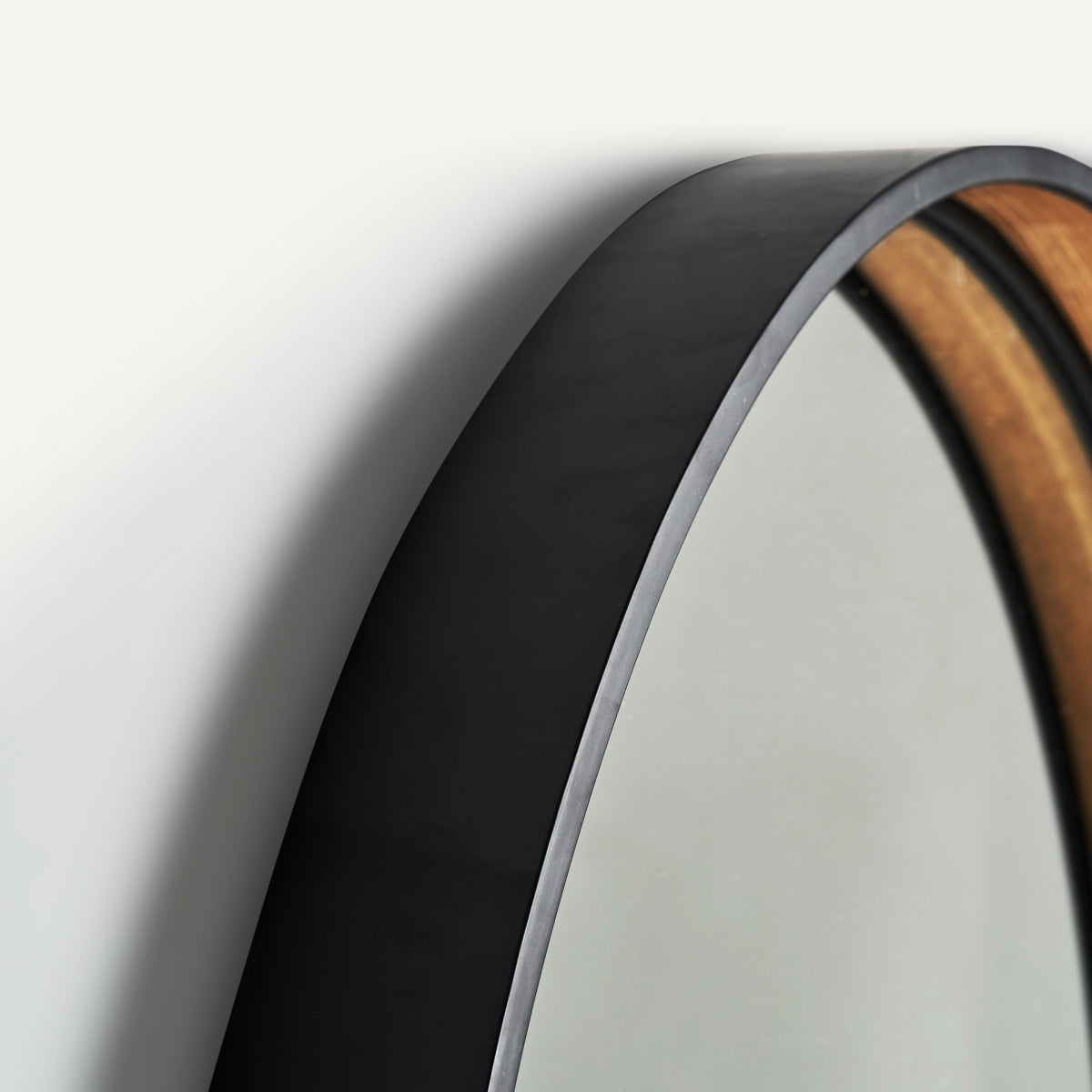 Primer plano del Espejo redondo en hierro negro y DM (100x100 cm) Aimar, con marco grueso negro y efecto madera de estilo art déco, montado sobre una pared de color claro.