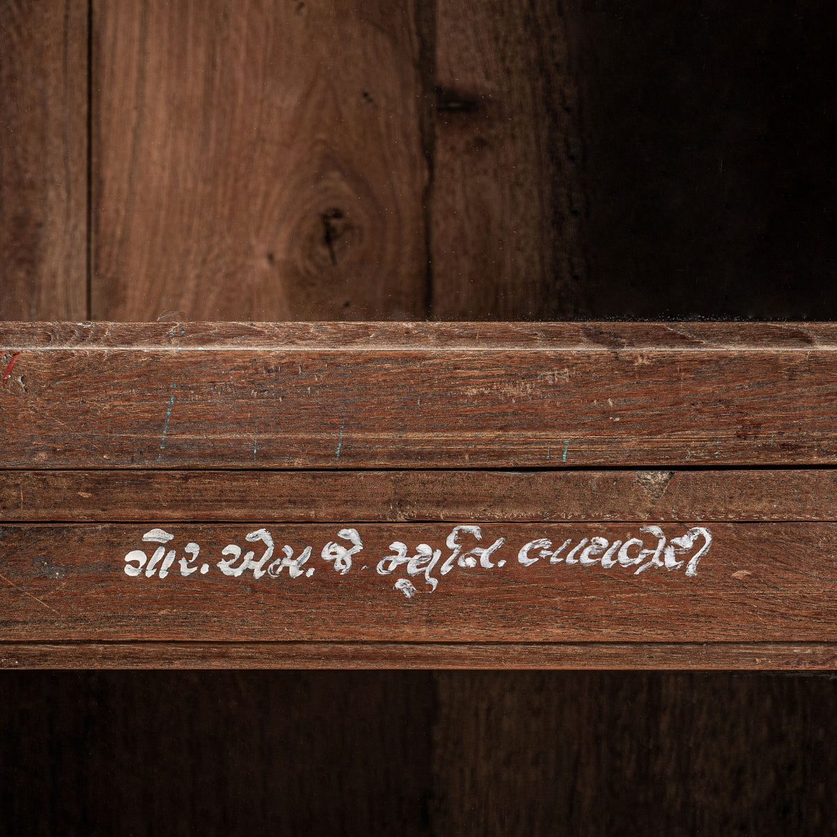 Un primer plano de la vitrina rústica en madera reciclada Jekye, su superficie de madera de mango muestra una escritura gujarati blanca sobre un fondo marrón cálido, creando un ambiente acogedor.