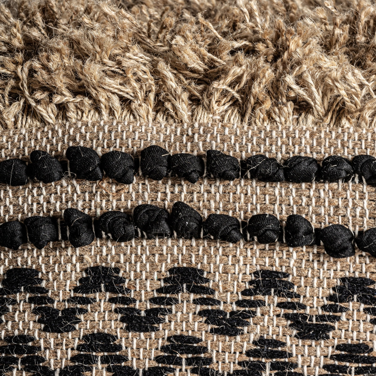 Presentamos un primer plano del puff cuadrado de yute y algodón Vassley, con un tejido con flecos peludos. Cuentas negras y un llamativo patrón en zigzag negro sobre un fondo beige destilan un inconfundible encanto bohemio.