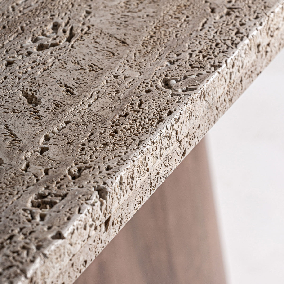 Primer plano de la mesa de comedor en travertino y madera Sannum, que presenta una superficie de piedra texturizada detallada con varios agujeros y ranuras, ideal para un entorno inspirado en el Art Deco.