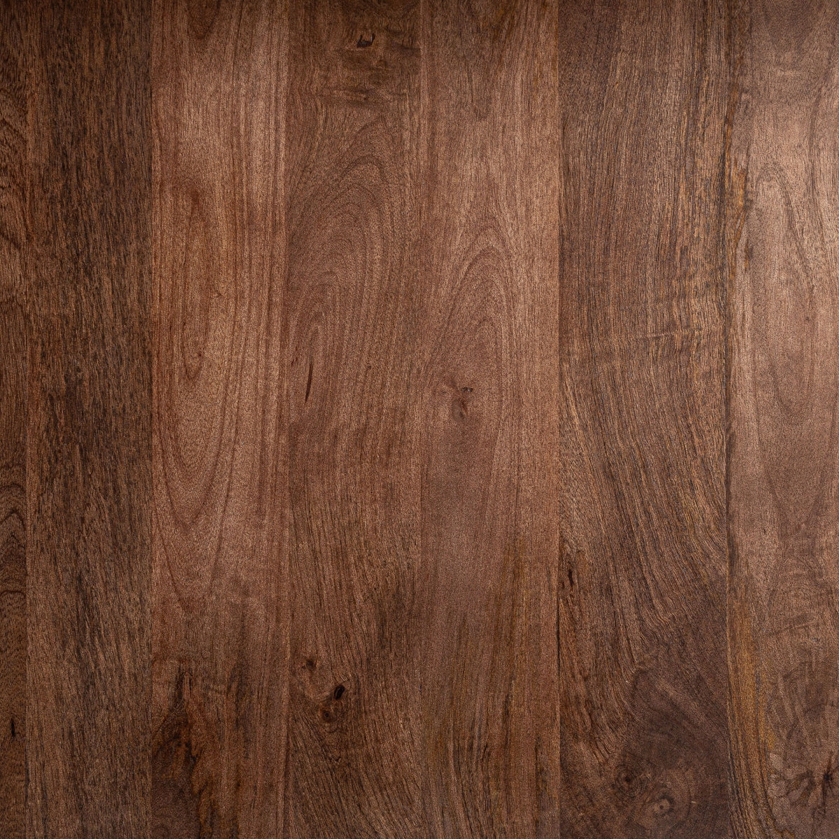 La mesa de comedor Sannum presenta una textura de madera marrón oscuro con patrones de vetas visibles y ligeras imperfecciones, que recuerdan a un acabado travertino, mostrando variaciones naturales en el color y los detalles.