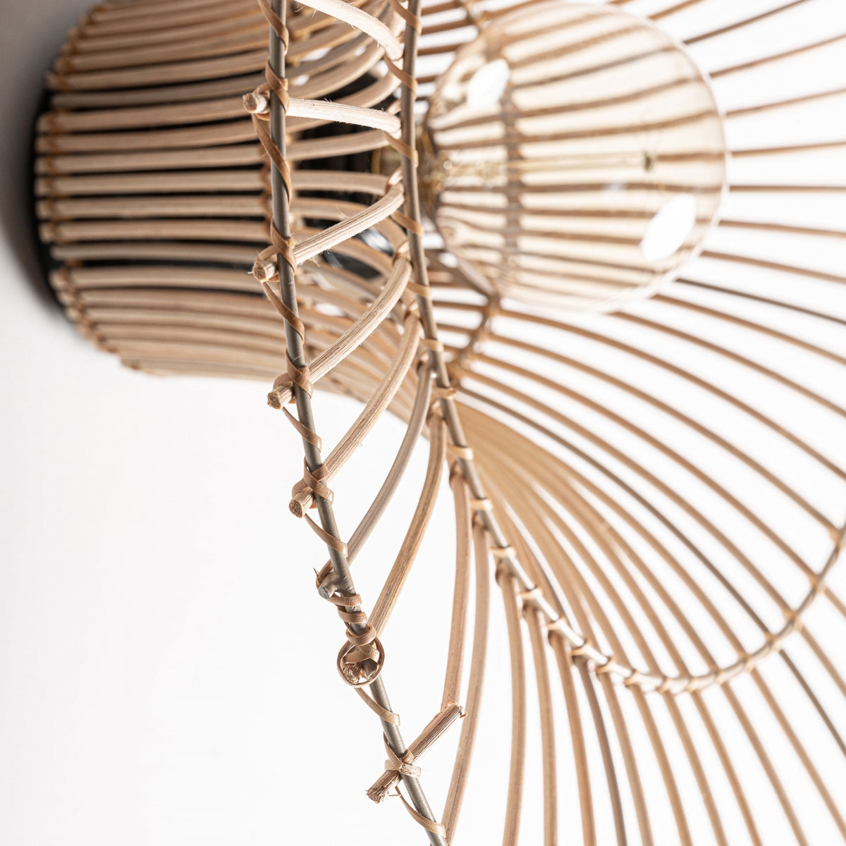 Primer plano del Aplique de pared en hierro y ratán Temir, que presenta una pantalla circular de ratán tejido y una bombilla visible: una elegante lámpara de pared que combina un diseño intrincado con una sutil inspiración Art Déco.