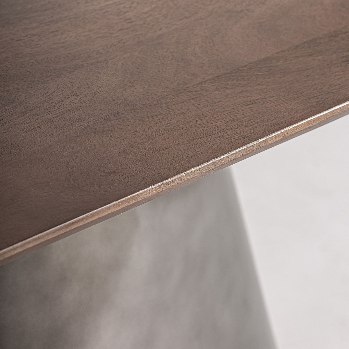 El primer plano del borde de una mesa de comedor rectangular en madera y acero Warhem resalta la exquisita madera de mango con un acabado suave, sobre un fondo gris claro.