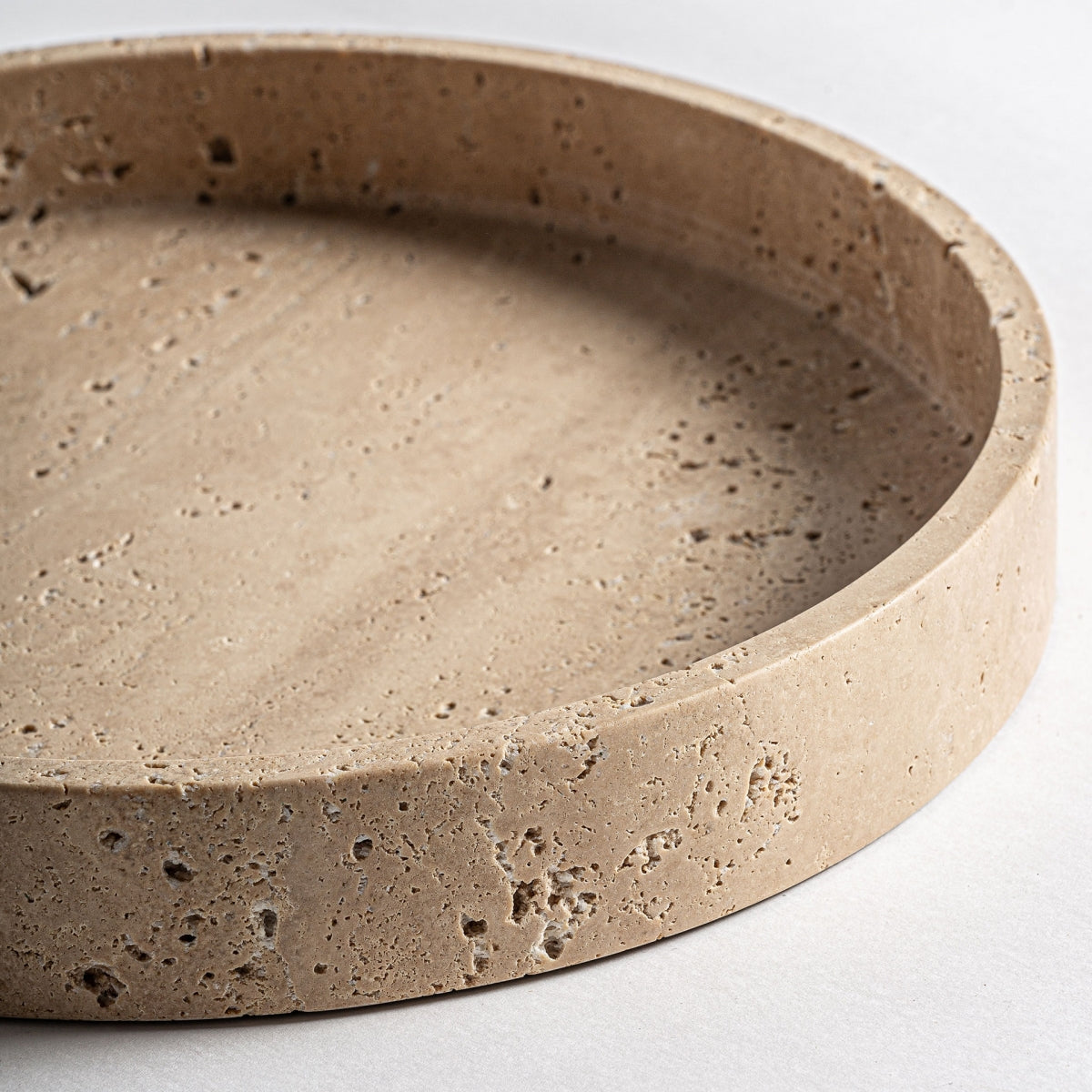 El centro de mesa en mármol beige Tetbury S, de forma redonda con borde elevado y textura natural, aporta elegancia y funcionalidad al espacio e inspira detalles art déco sobre una superficie clara.