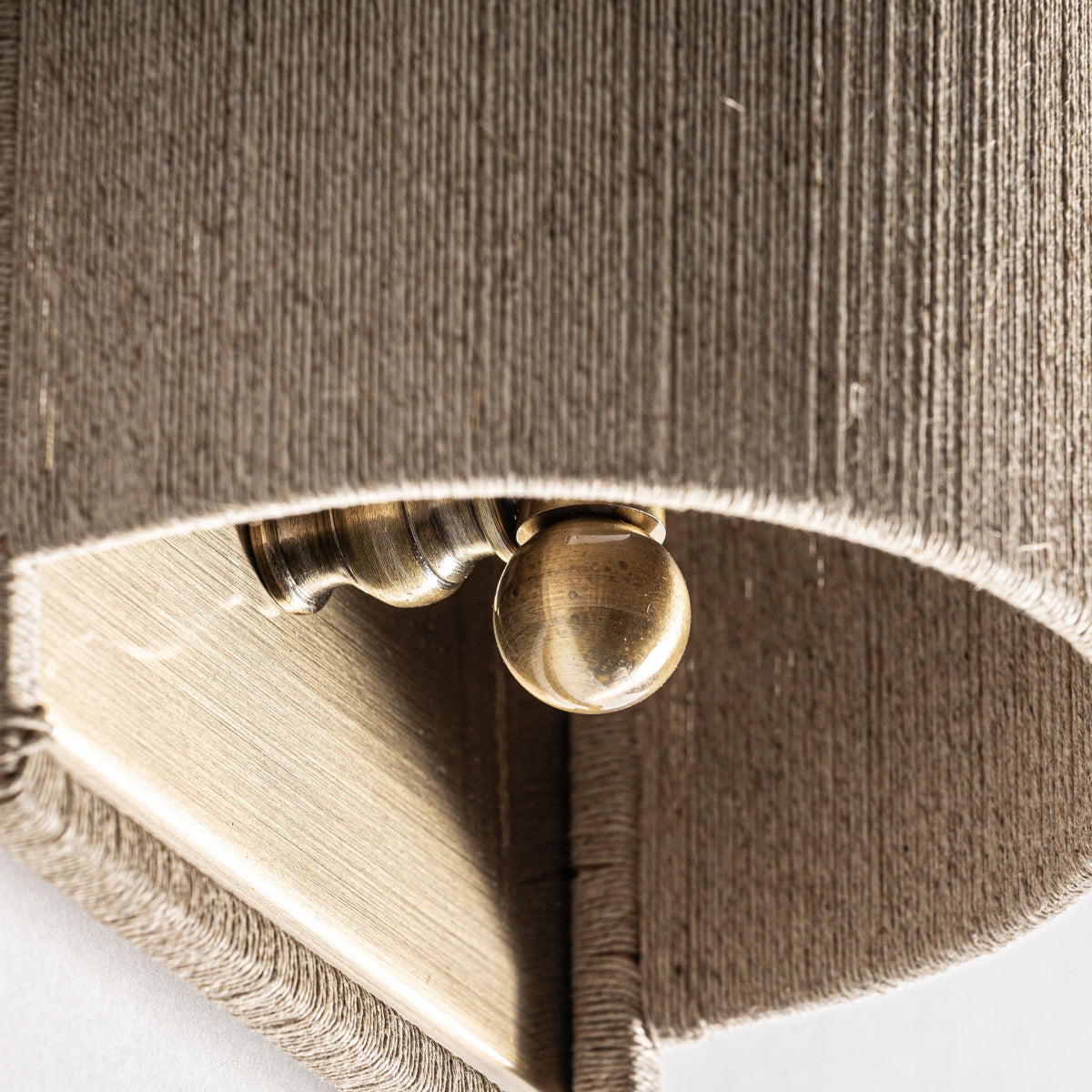 Primer plano del Aplique de pared en hierro y cuerda Rives S, que muestra su diseño detallado de hierro y cuerda sobre una tela marrón texturizada para una apariencia elegante inspirada en el art déco.