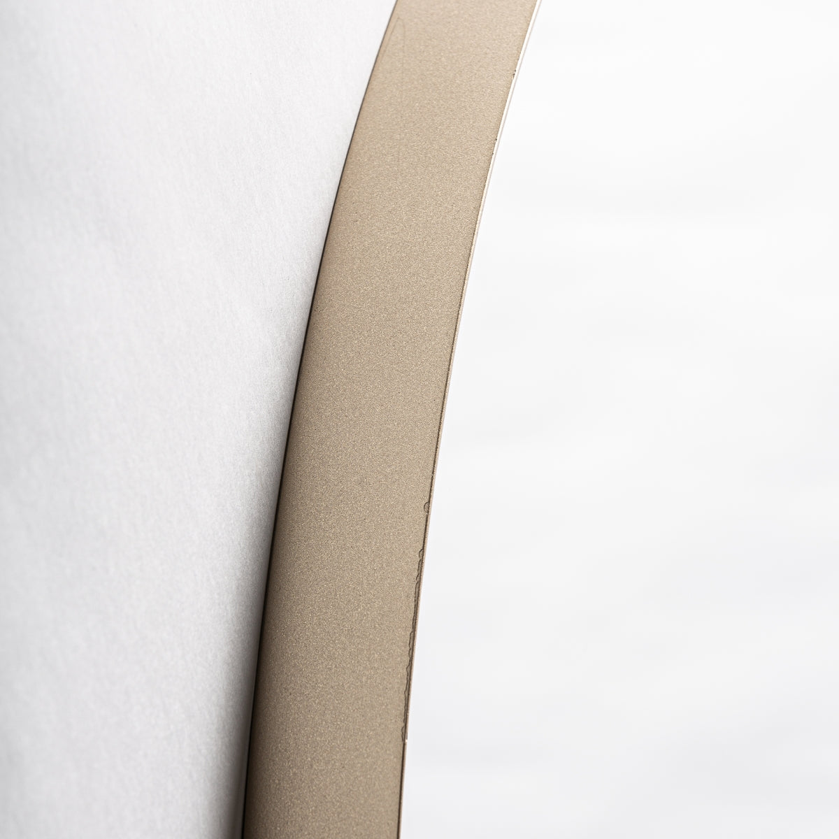 Primer plano de un borde beige suave y curvado del Espejo redondo en hierro oro (Ø90 cm) Nuria sobre un fondo blanco suave, evocando líneas limpias y una textura mínima, perfecto para una decoración de interiores inspirada en el art déco.