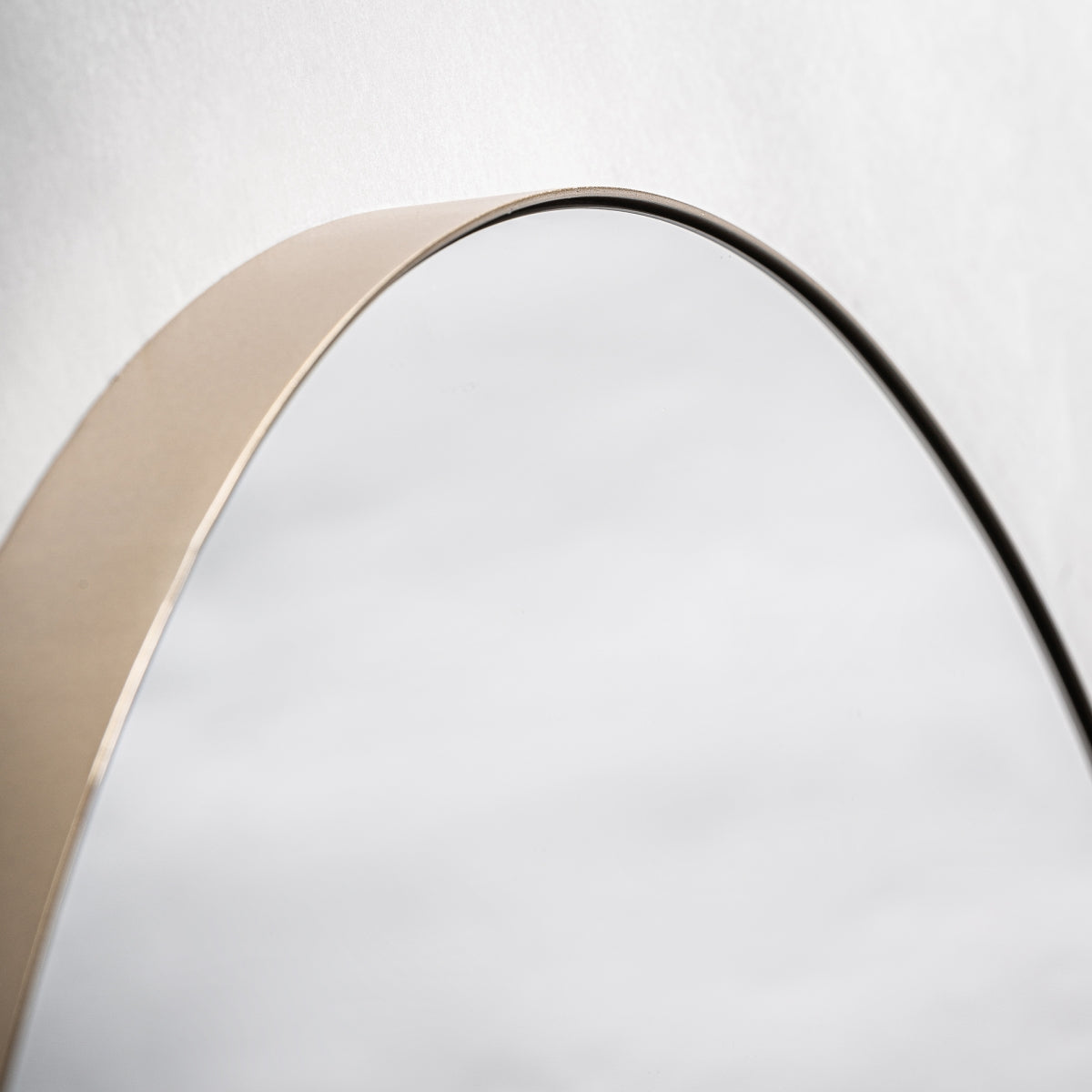 Primer plano del borde superior del Espejo redondo en hierro oro (Ø90 cm) Nuria, que presenta un fino marco metálico sobre un fondo blanco, ideal para decoración de interiores moderna.