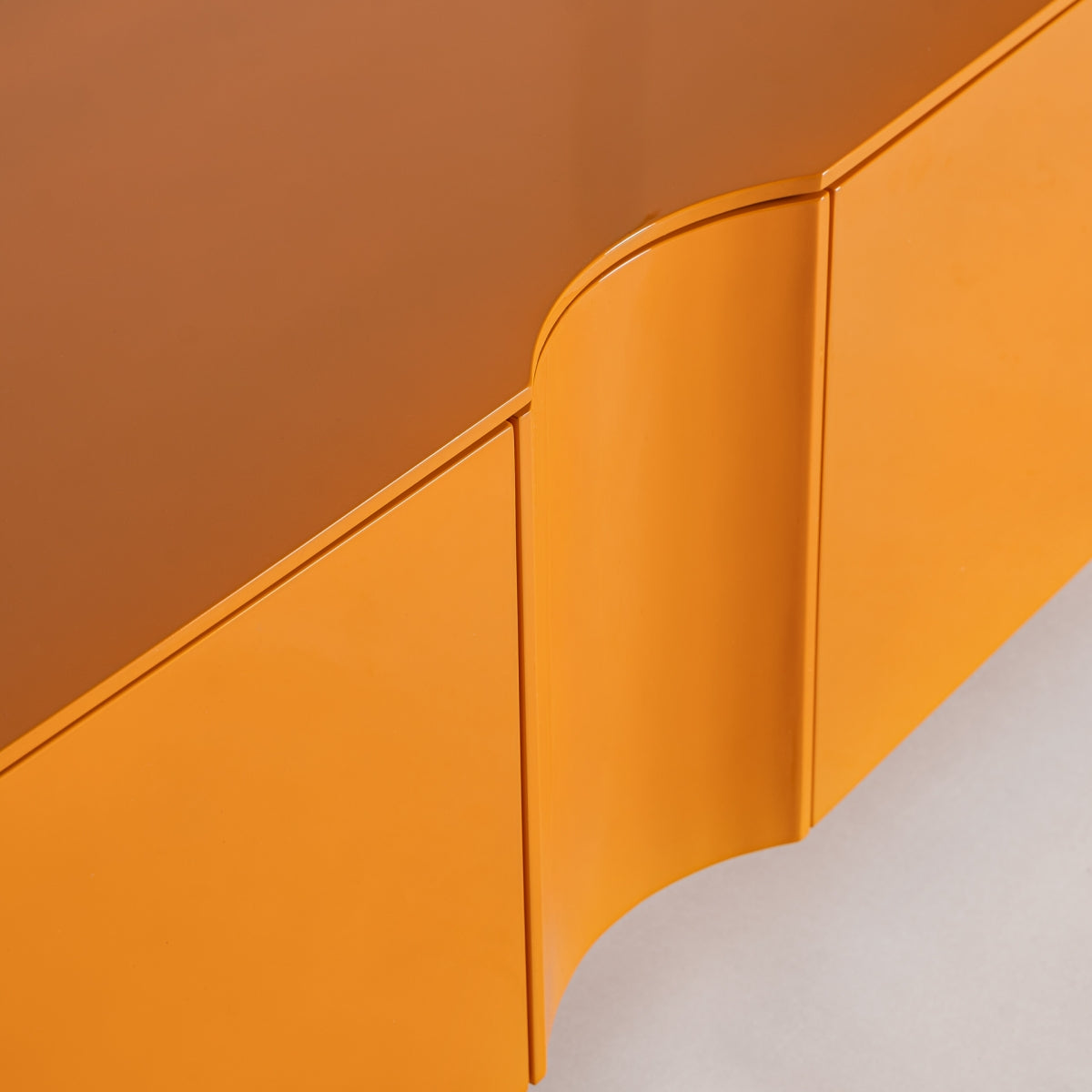 El mueble TV en madera DM y hierro Mirkov cuenta con un mueble esquinero de color naranja con un diseño suavemente curvado y un acabado lacado naranja brillante, que contrasta bellamente con un fondo gris claro.