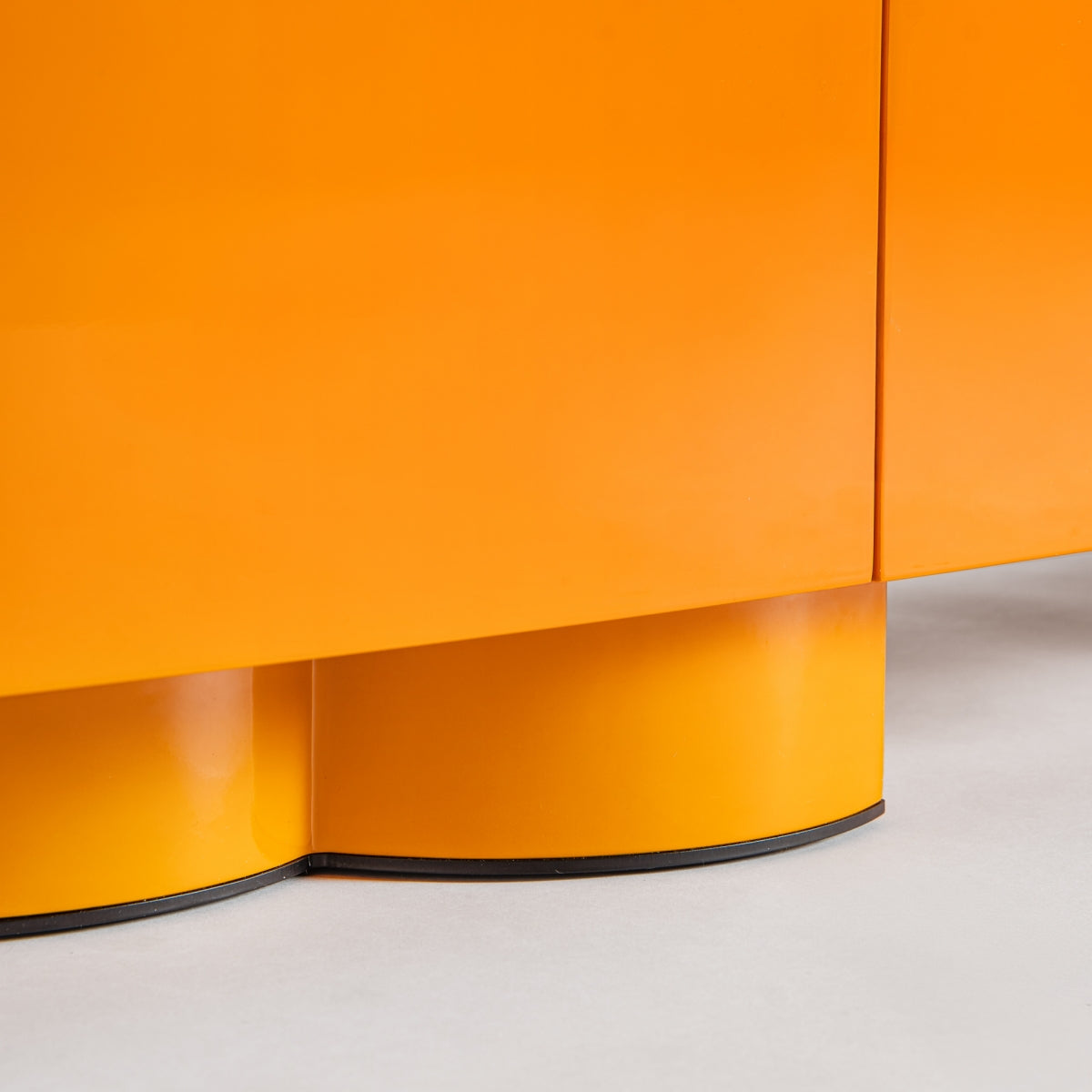 Primer plano de un mueble TV naranja de madera DM y hierro Mirkov con una base redondeada única sobre un suelo gris claro. Su acabado lacado naranja y su diseño minimalista le aportan un toque moderno, convirtiéndolo en un complemento elegante para cualquier habitación.