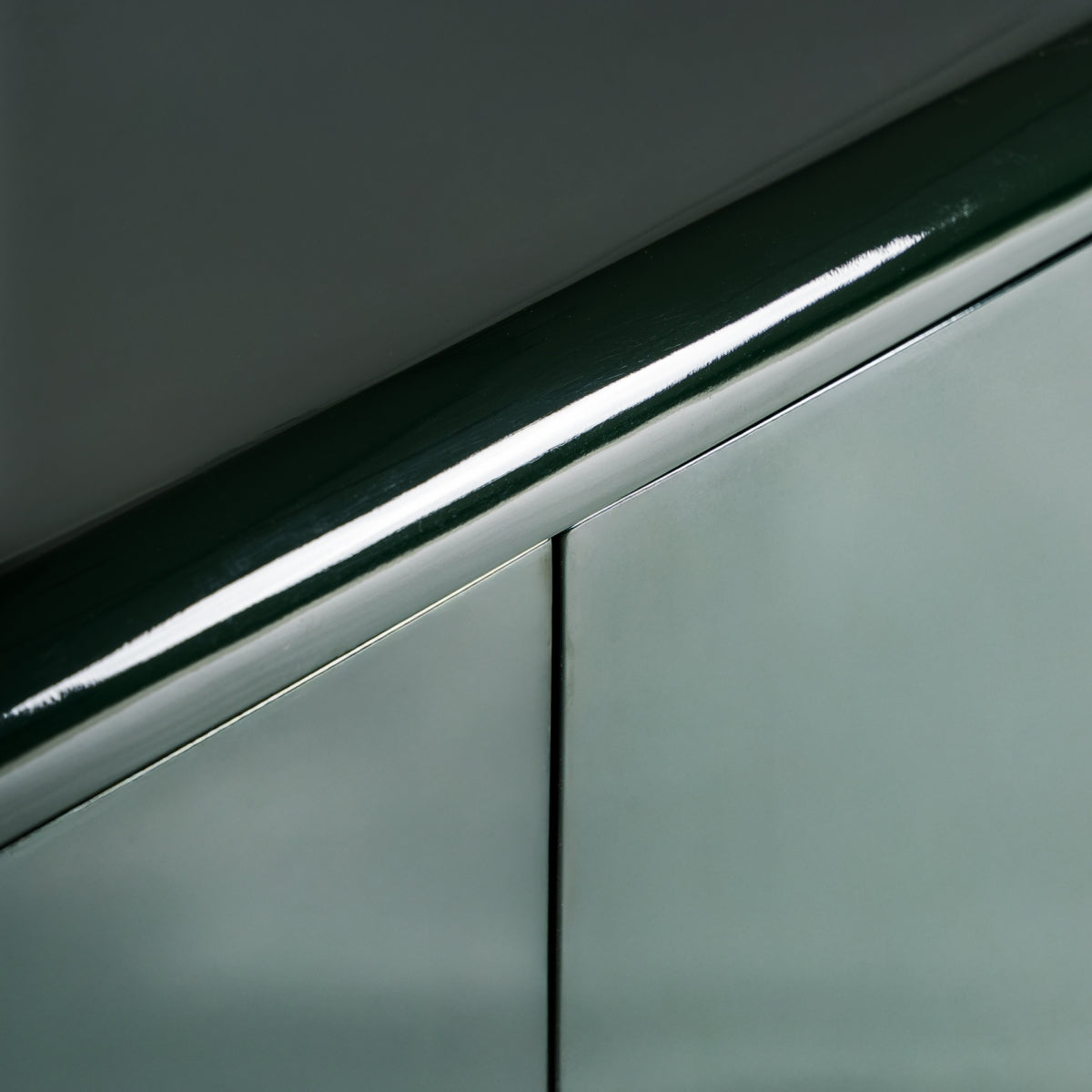 Primer plano de un pasamanos verde brillante sobre paneles de pared verde mate con una costura vertical, formando una composición inspirada en el Art Decó, una combinación ideal para el Aparador en DM verde y acero inoxidable (180x45 cm) Gory.