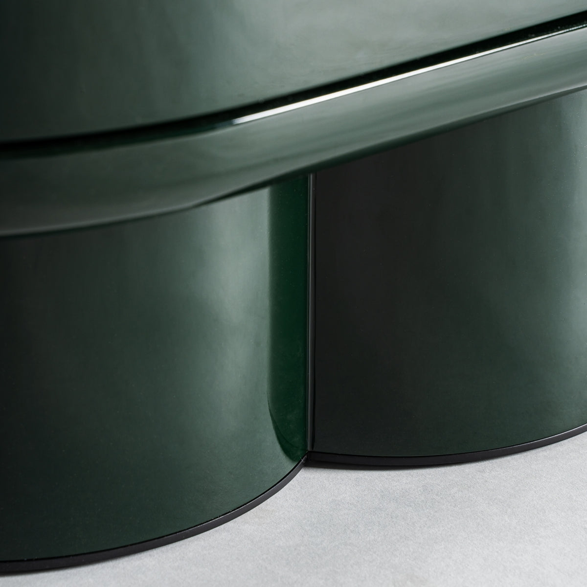 Primer plano de la base curva del Aparador en DM verde y acero inoxidable (180x45 cm) Gory, de color verde oscuro brillante, colocado sobre una superficie de color claro.