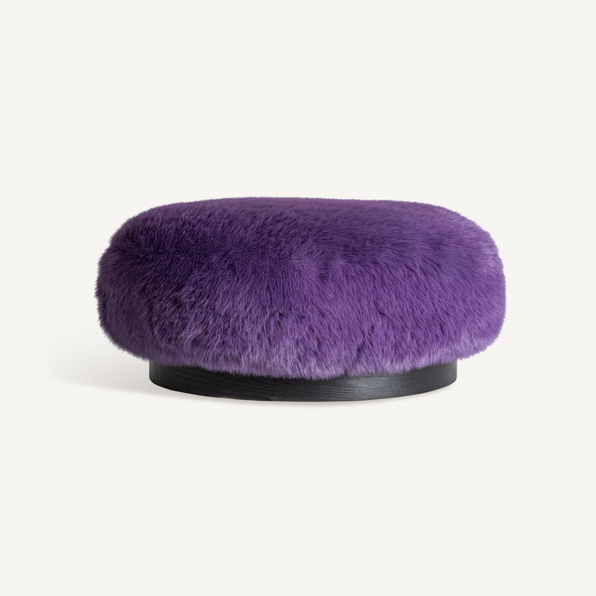 El Puff redondo tapizado en peluche Tropez presenta un cojín de felpa morado sobre una base circular negra, resaltando su textura peluda contra un fondo blanco liso.