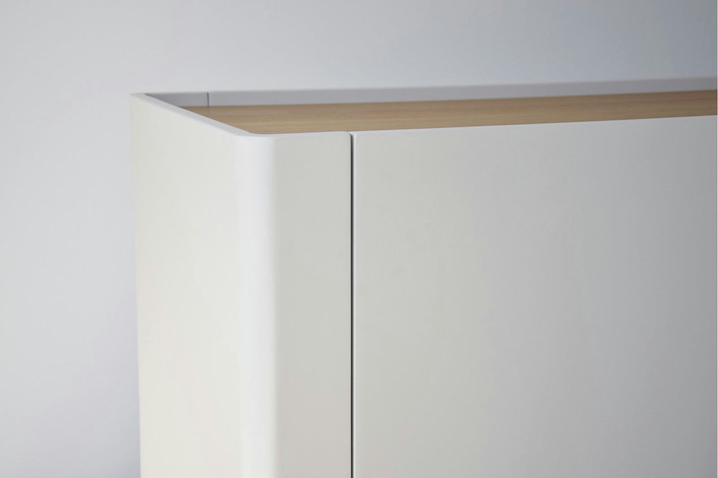 El Aparador bajo Gris Arena y Madera de Roble Elegance presenta un diseño minimalista con su base blanca y cubierta de madera clara, creando una apariencia moderna contra una pared sencilla.