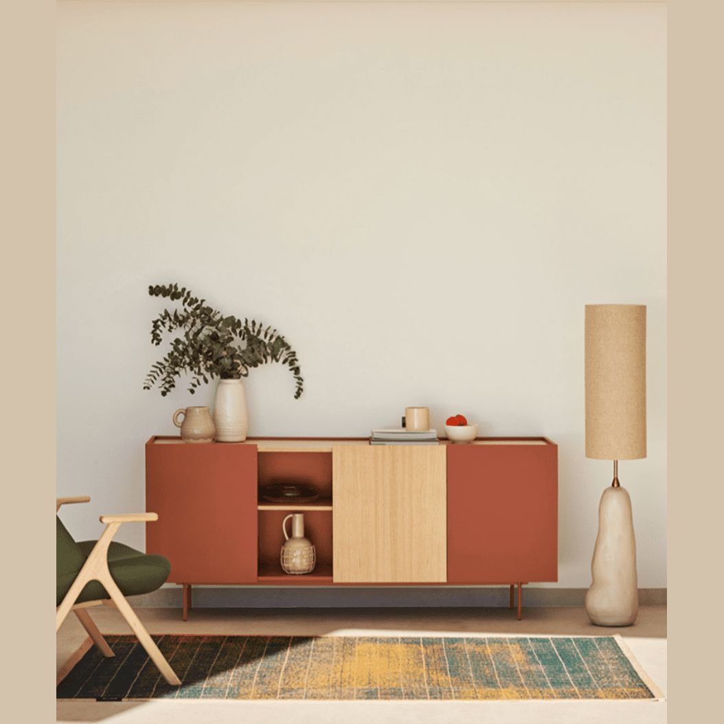 Esta sala de estar moderna de mediados de siglo exhibe el versátil Aparador moderno Otto 3P3C, un impresionante aparador rojo y de madera. Realzado por una lámpara alta, plantas decorativas y una silla verde, se encuentra sobre una alfombra colorida, lo que agrega un encanto vibrante al espacio.