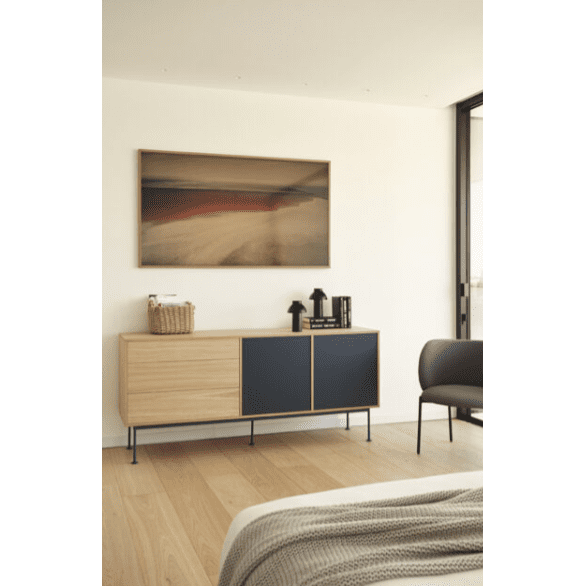 Una habitación de estilo industrial moderno muestra el elegante Aparador moderno Yoko 2P3C debajo de una obra de arte abstracta. Una canasta tejida realza la textura junto a la máquina de café y la silla. Los pisos de madera clara, las paredes neutrales y una esquina de cama organizada de manera inteligente garantizan un almacenamiento eficiente en todo el espacio.