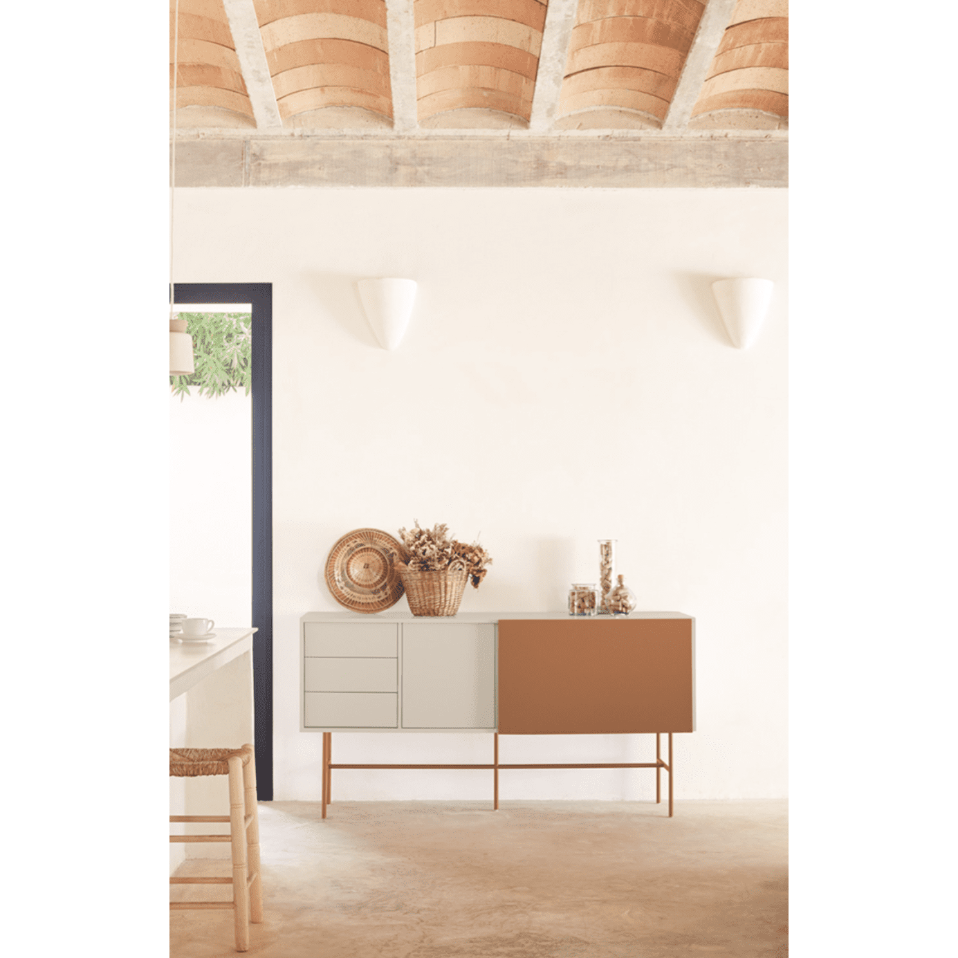 El Aparador moderno con Puerta Corredera Nube 2P3C, inspirado en Cambres Design, presenta paneles de color gris claro y marrón sobre una pared blanca. Está adornado con plantas y frascos secos, debajo de un techo de ladrillos de terracota curvado que complementa su elegancia chic.
