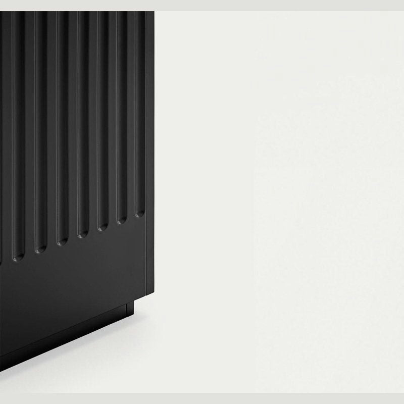 Primer plano del Aparador moderno con Puertas Doric 3P3C, que muestra su superficie vertical acanalada negra que recuerda al diseño escultórico sobre un fondo blanquecino liso.