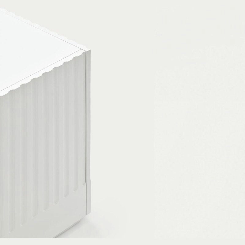 Primer plano de un objeto rectangular acanalado de color blanco sobre un fondo gris claro, que recuerda el estilo de diseño escultórico que se ve en la colección Aparador moderno con Puertas Doric 3P3C.