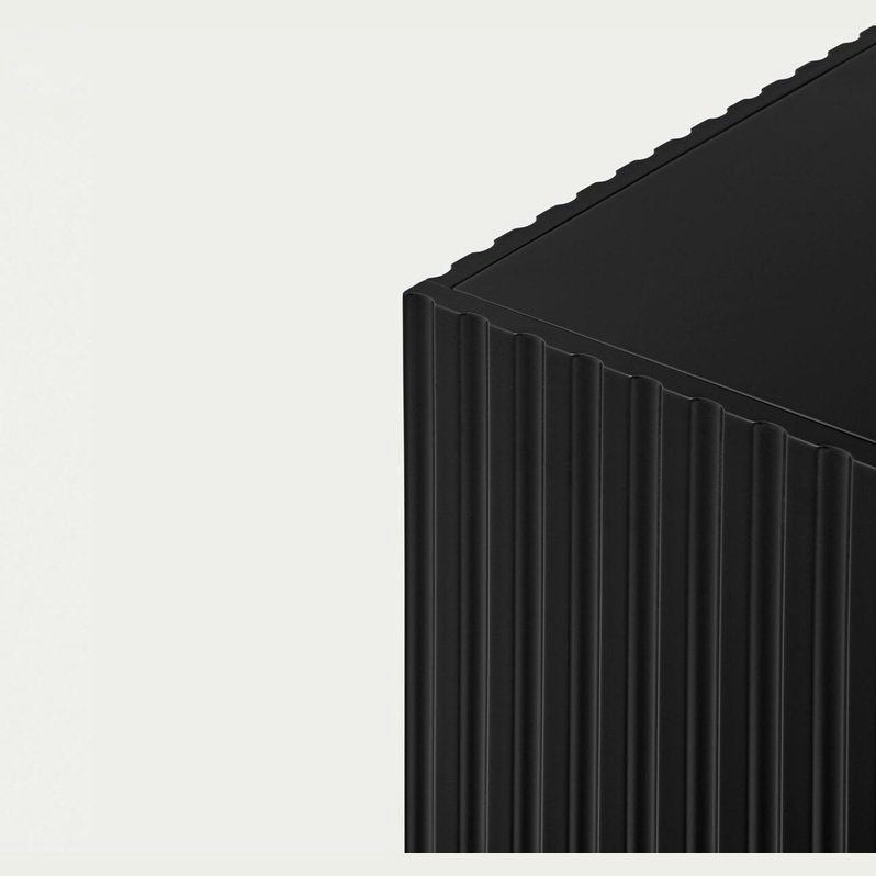 La imagen muestra una esquina de un objeto rectangular de textura acanalada y color negro, parecido a un Aparador moderno con Puertas Doric 4P4C, sobre un fondo gris claro.