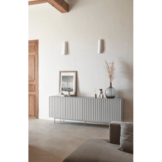 Una sala de estar minimalista muestra el Aparador moderno con Puertas Sierra 4P3C. Jarrones decorativos y una foto enmarcada lo adornan mientras la puerta y las vigas de madera agregan calidez, con dos luces de pared en la parte superior que realzan el diseño moderno industrial.