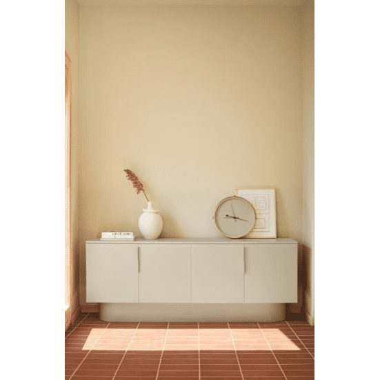Esta habitación minimalista muestra un Aparador moderno con Puertas Totem 4P3C en color beige, un jarrón blanco con flores secas y un reloj redondo. Un cuadro enmarcado cuelga encima, rezumando diseño de alta gama. Una iluminación cálida y un piso de baldosas completan la decoración.
