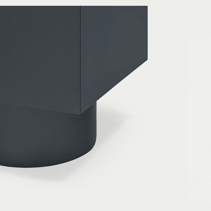 Primer plano del Aparador moderno con Puertas Totem 4P3C, que presenta un diseño geométrico gris oscuro con una parte superior rectangular y una base cilíndrica, sobre un fondo gris claro.