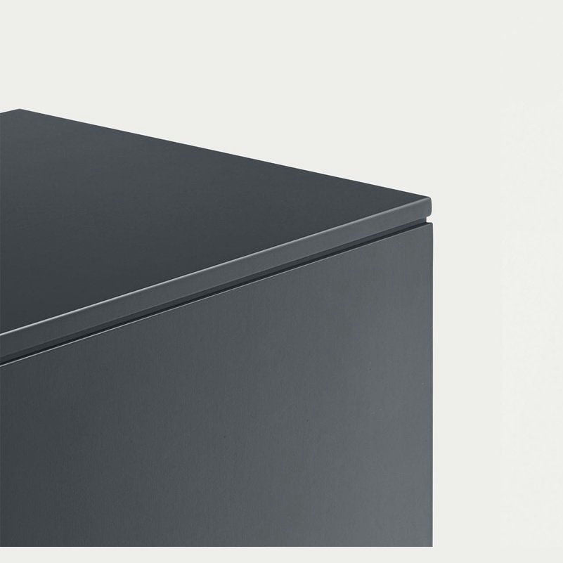 Primer plano de una esquina gris oscuro del Aparador moderno con Puertas Totem 4P3C sobre un fondo gris claro, resaltando sus bordes afilados y superficie lisa emblemática del diseño de alta gama.