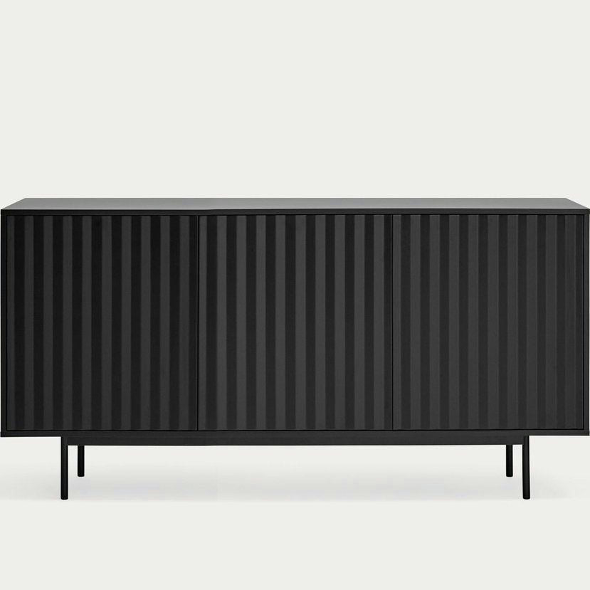 El Aparador pequeño con Puertas Sierra 3P3C presenta un diseño de rayas verticales acanaladas en color negro. Se apoya sobre cuatro patas delgadas que encarnan el estilo industrial moderno sobre un fondo claro.