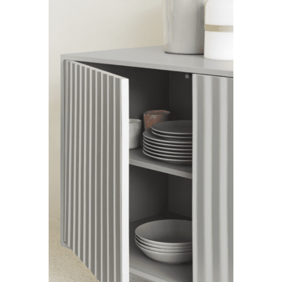 El Aparador pequeño con Puertas Sierra 3P3C está parcialmente abierto y exhibe pilas de platos grises dentro de sus puertas a rayas. Dos jarrones se encuentran sobre el elegante gabinete, lo que resalta su diseño moderno y su amplio espacio de almacenamiento.