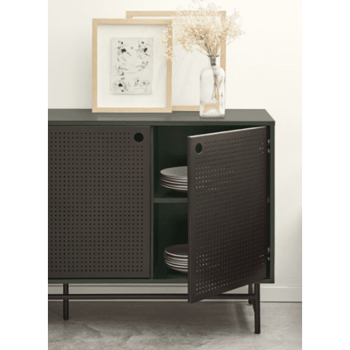 El Aparador pequeño en Metal y DM Punto 2P4C en color verde oscuro presenta una puerta corrediza parcialmente abierta con placas apiladas. Dos obras de arte enmarcadas y un jarrón con flores secas adornan la parte superior, mostrando un estilo industrial y un diseño moderno.